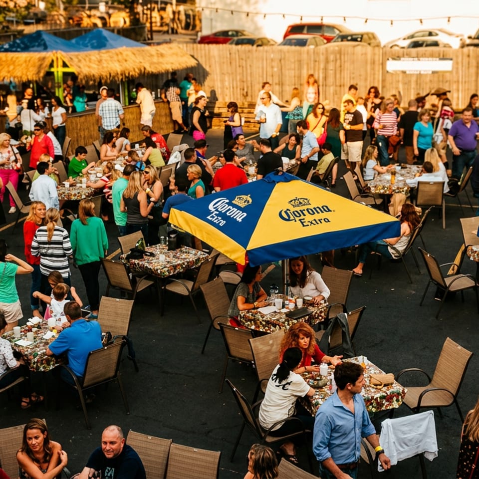 Crowded outdoor restaurant patio with diners, food tables, live music, and colorful Corona beer umbrellas.