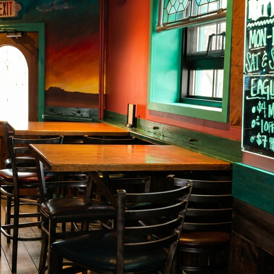 Colorful restaurant dining area with wooden tables, black chairs, scenic mural, window, and handwritten beer specials board.