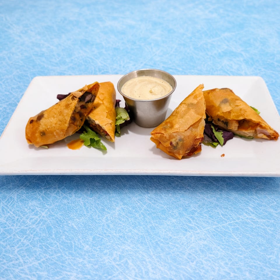 Golden-brown stuffed pastry triangles served with creamy dipping sauce and fresh herbs on a white rectangular plate.